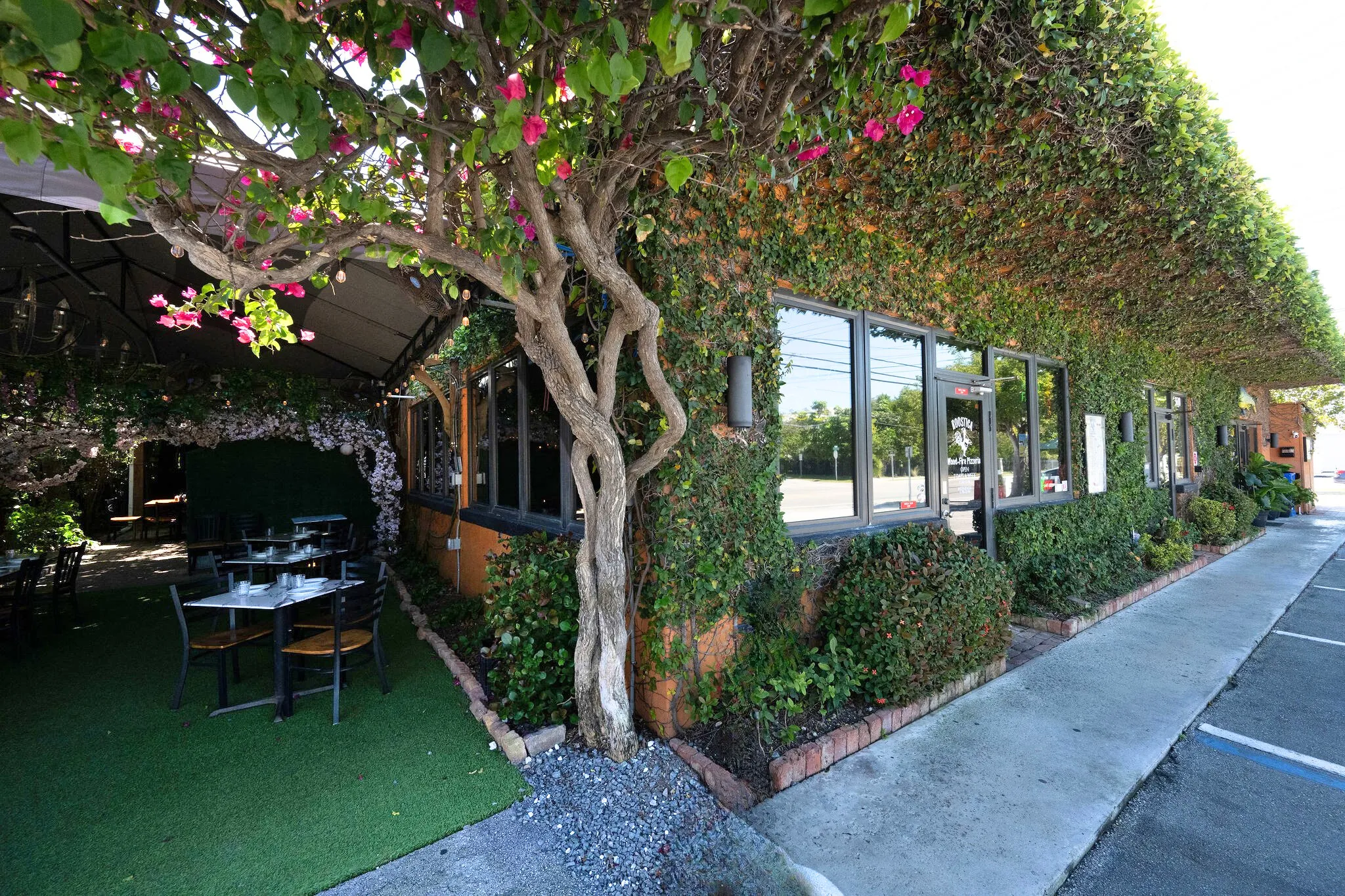 Roostica Wood-Fire Pizzeria exterior: vine-covered building, patio seating