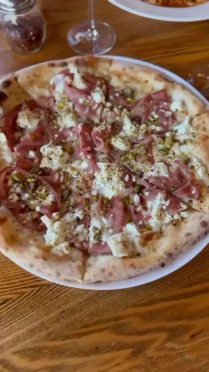 Wood-fired pizza with prosciutto and fresh cheese on a wooden table
