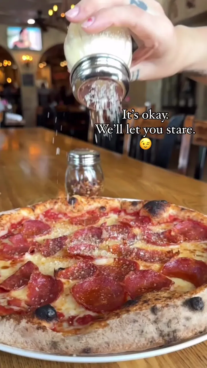 Sprinkling cheese over a fresh pepperoni pizza at Roostica